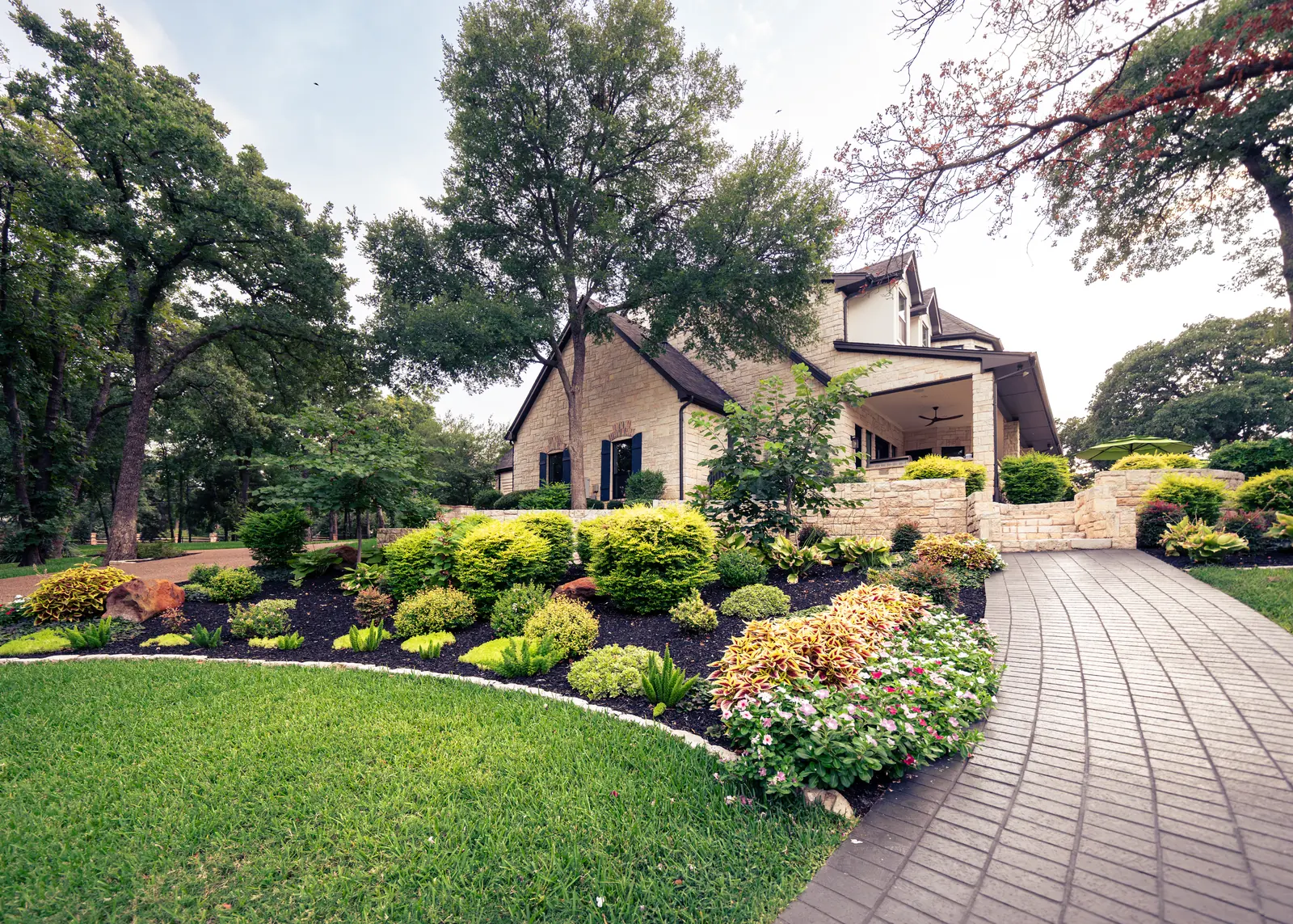 Manicured front lawn with colorful landscaped beds, stone edging, and a paver driveway at a Fort Worth home by Greenview Landscaping
