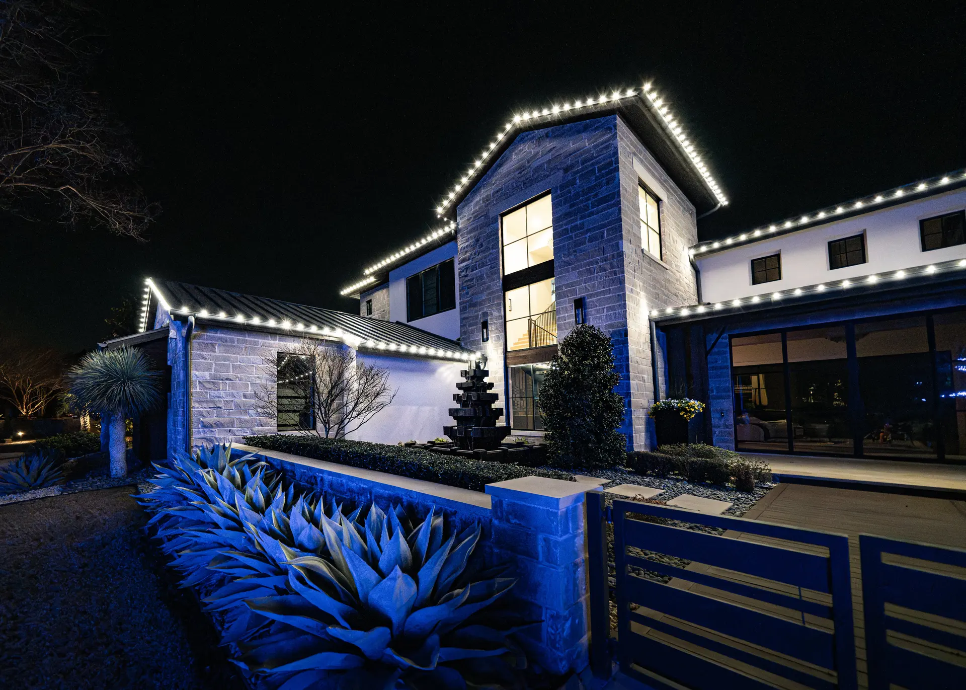 Modern stone home with warm white roofline lights installed by Greenview, lit at night